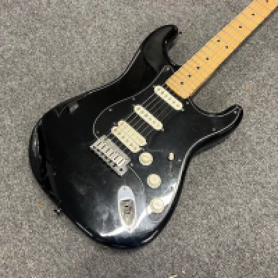 A 2004 USA Fender Stratocaster Electric Guitar in Black with HSS pickup configuration. Maple fingerboard with some significant fretwear All original parts. Condition Fair with extensive damage to paint finish on the back and sides. Missing vibratro arm. Some tarnishing to brightwork. Comes with original Fender indent case.