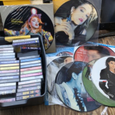 A collection of LPs and 12" picture discs plus a box of audio cassettes.