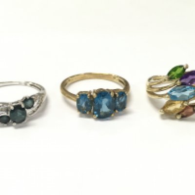 Three 9ct gold rings including a teal sapphire and white stone set white gold ring size R, Blue topaz trilogy ring size R, multi gem ring size O. 8.2g total weight. Postage category A
