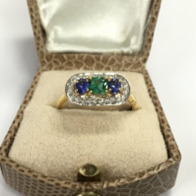 14ct yellow gold deco inspired ring set with a square cushion cut emerald and oval tanzanite surrounded by diamonds. Size P