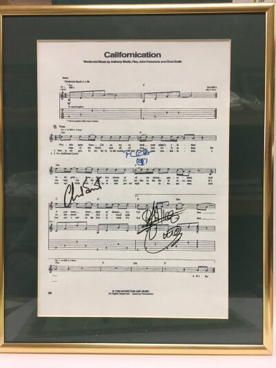 A framed and glazed signed Red Hot Chili Peppers Californication music sheet bearing the autographs of Anthony Kiedis, Flea and Chad Smith with COA. Approx 29cm x 36cm.