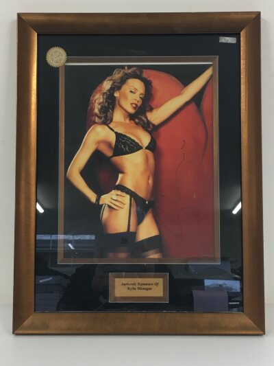 A framed and glazed signed photo of Kylie Minogue, approx 48.5cm x 63cm plus a box of pop music related items comprising a Britney Spears signed display (faded), an Abba official photo book, framed photos etc.
