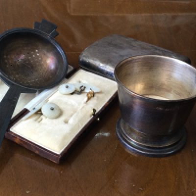A silver cigarette case and tea strainer