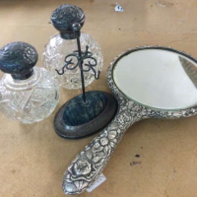 A silver hand mirror, two silver topped glass perfume bottles and a hat pin stand