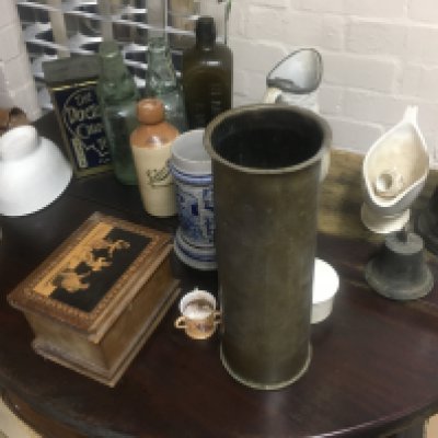 A box containing glass bottles advertising various ceramics and a pewter jug.