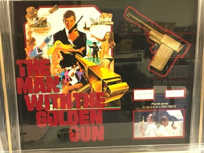 James Bond The Man With The Golden Gun. A dual signed display featuring the signatures of Roger Moore and Christopher Lee with poster artwork and a resin 1/1 copy of Scramanga's golden gun. All housed in a frame with COA to reverse. Approx 80cm x 70cm.