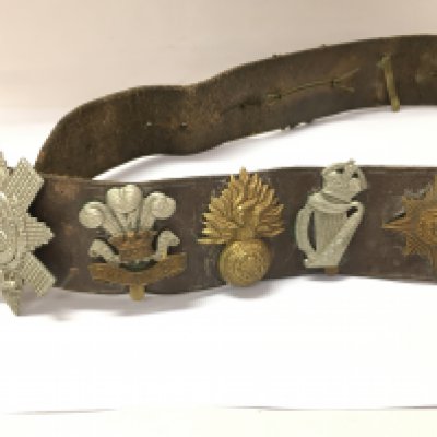 A collection of assorted cap badges fixed to a vintage belt. Postage B